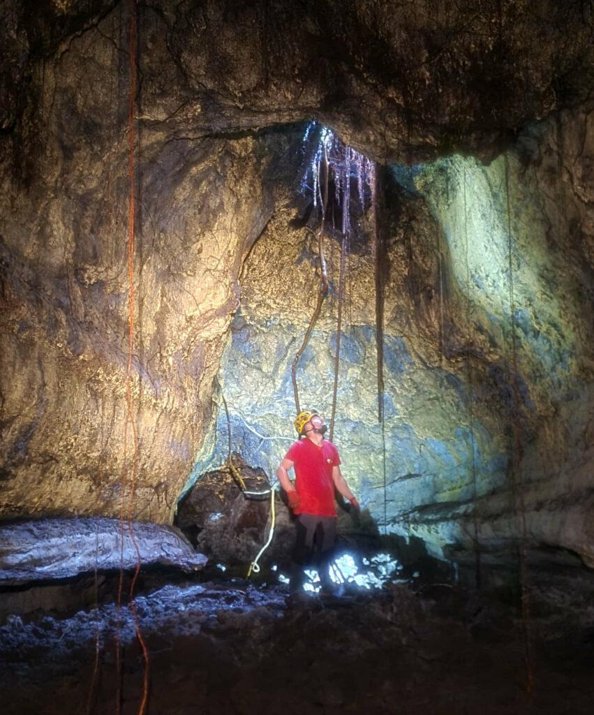 Spéléologue explorant une salle du tunnel de lave de Citron Galet à La Réunion avec puits de lumière